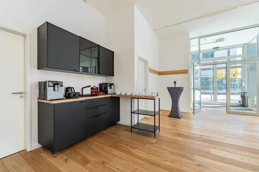 Kaffeebereich des Instituts mit Kaffeemaschinen, Tassen auf der Holztheke, Garderobe und Blick zum Eingang.